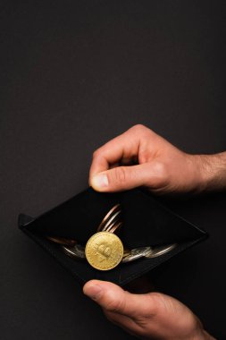 KYIV, UKRAINE - 26 Nisan 2022: Siyah arka planda bitcoin bulunan cüzdan açan adam görüntüsü