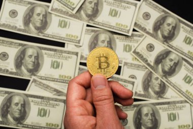 KYIV, UKRAINE - 26 Nisan 2022: Siyah arka planda bulanık dolarların yanında bitcoin tutan adam görüntüsü