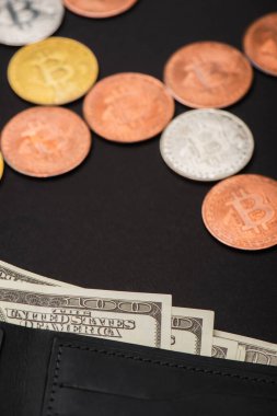 KYIV, UKRAINE - 26 Nisan 2022: Siyah arkaplanda bulanık bitcoinlerin yanında dolarlarla cüzdanın görüntüsünü kapat