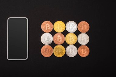 KYIV, UKRAINE - 26 Nisan 2022: Siyah üzerine izole edilmiş kripto paraların yanındaki boş ekran ile akıllı telefonun üst görünümü 