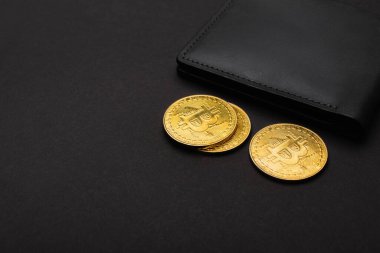 KYIV, UKRAINE - 26 Nisan 2022: Siyah arka planda cüzdanın yanındaki altın bitcoinlerin görüntüsünü kapat