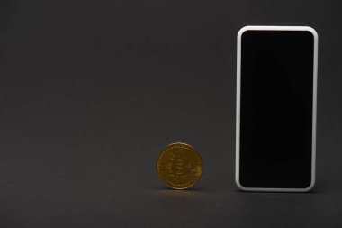 KYIV, UKRAINE - 26 Nisan 2022: Siyah arka planda boş ekranlı altın bitcoin ve cep telefonu