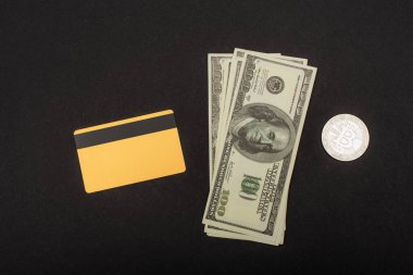 KYIV, UKRAINE - 26 Nisan 2022: Kredi kartı yakınındaki dolarların üst görünümü ve siyah arka plandaki gümüş bitcoin