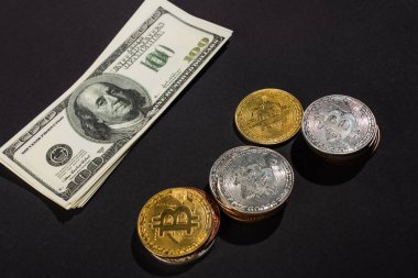 KYIV, UKRAINE - 26 Nisan 2022: Siyah arka planda altın ve gümüş bitcoins yakınlarındaki dolar banknotlarının yüksek açılı görünümü