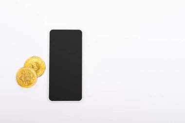 KYIV, UKRAINE - 26 Nisan 2022: Akıllı telefonun yanındaki beyaz ekranlı altın paraların üst görünümü 