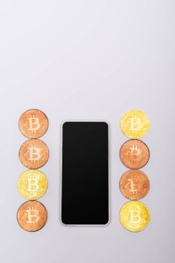 KYIV, UKRAINE - 26 Nisan 2022: Gri arkaplanda boş ekranla cep telefonunun yanındaki kripto para biriminin üst görüntüsü 