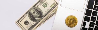 KYIV, UKRAINE - 26 Nisan 2022: Dizüstü bilgisayardaki altın bitcoin 'in beyaz arkaplandaki dolarlara yakın üst görünümü, afiş