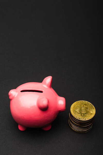 KYIV, UKRAINE - APRIL 26, 2022: Close up view of pink piggy bank near bitcoins on black background