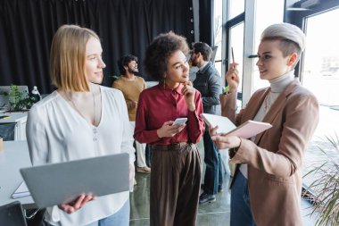 Defteri ve kalemi olan kadın reklam ajansında çok ırklı iş arkadaşlarıyla konuşuyor.
