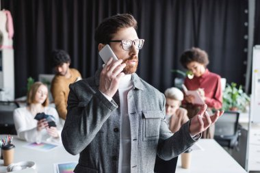 Gözlüklü reklamcı, çok kültürlü iş arkadaşlarının yanında akıllı telefondan konuşuyor. 