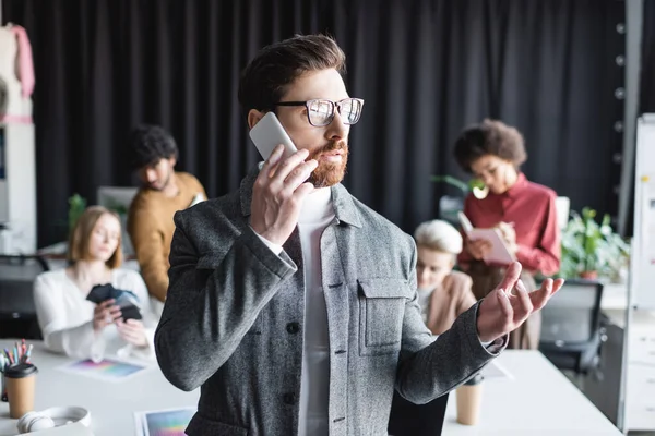 Διαφημιστής Γυαλιά Ηλίου Που Μιλάει Smartphone Κοντά Θολή Πολυπολιτισμικούς Συναδέλφους — Φωτογραφία Αρχείου