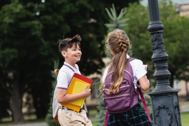 Gülümseyen Asyalı okul çocuğu dışarıda sınıf arkadaşının yanında not defteri tutuyor. 
