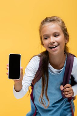 Sırt çantası ve sarı ekranda boş ekranlı akıllı telefon tutan pozitif okul çocuğu. 