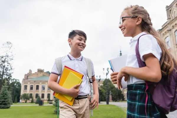 带着笔记本和背包站在室外笑多族裔学童 — 图库照片