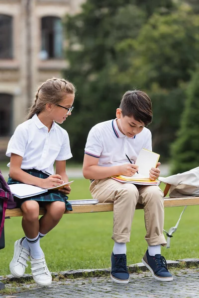 Asian Schoolboy Writing Notebook Friend Bench Outdoors — Stock Photo, Image