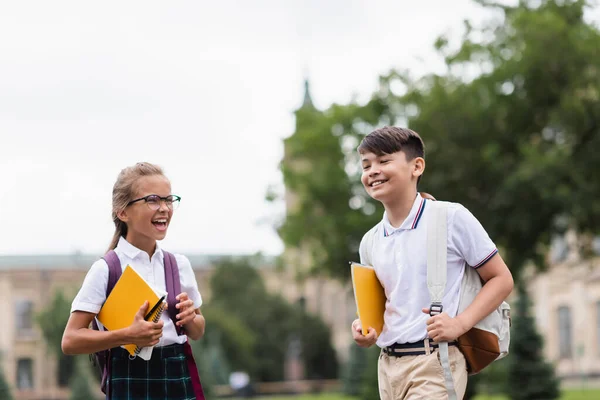 Pozytywne Międzyrasowe Dzieci Szkolnymi Notatnikami Trzymające Plecaki Świeżym Powietrzu — Zdjęcie stockowe
