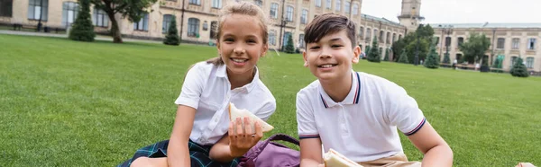 Irklar arası çocuklar ellerinde sandviçlerle parktaki çimenlikte kameraya gülümsüyorlar. 