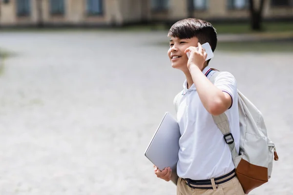 笑顔アジアの学生がノートパソコンを持ち 屋外で携帯電話で話す — ストック写真
