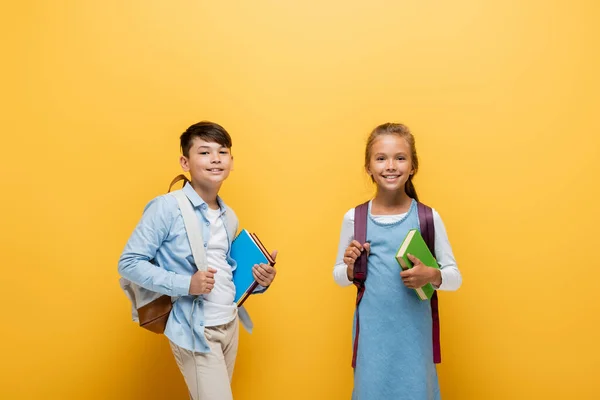 Glimlachen Interraciale Schoolkinderen Met Boeken Rugzakken Gele Achtergrond — Stockfoto