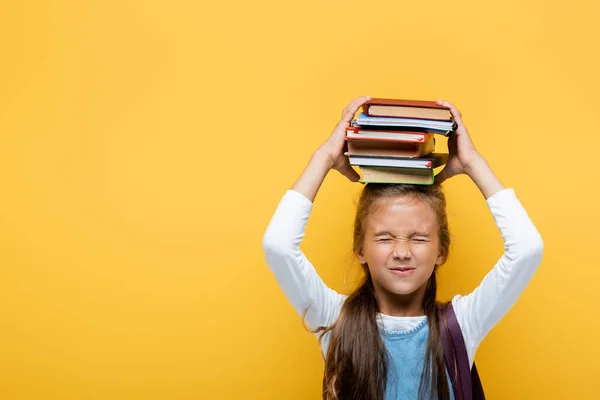 Positive schoolkid holding books and closing eyes isolated on yellow