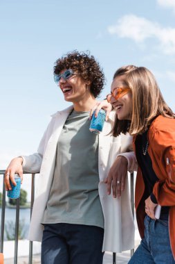 Dışarıda soda kutularıyla gülümseyen genç ve şık bir çift.