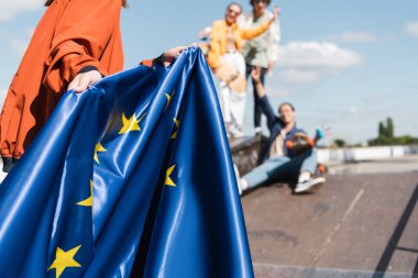 Açık havada bulanık arkadaşlarının yanında Avrupa Birliği bayrağı taşıyan bir kadının kısmi görüntüsü