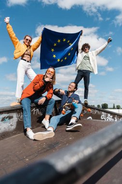 Paten parkında Avrupa Birliği bayrağı taşıyan mutlu çok kültürlü arkadaşlar