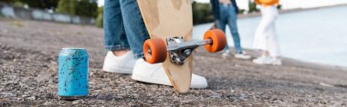partial view of woman with longboard near soda can on asphalt and blurred friends, banner clipart
