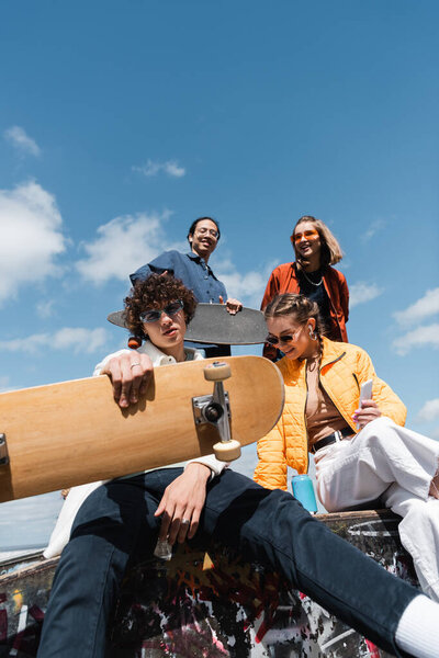 low angle view of young friends with skateboard and longboard against blue cloudy sky