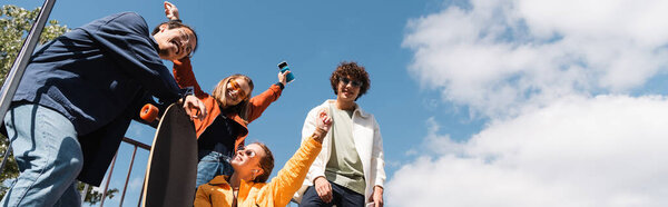 низкий угол зрения счастливых женщин, показывающих успех жест рядом с межрасовыми фигуристами, баннер