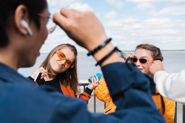 cheerful women in trendy sunglasses looking at man on blurred foreground