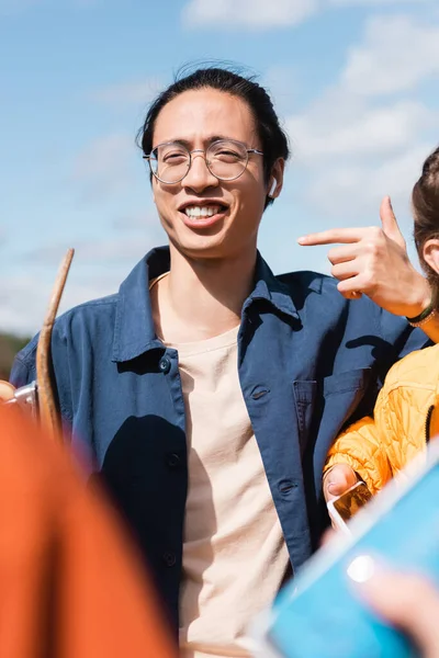Feliz Asiático Hombre Gafas Apuntando Con Dedo Cerca Borrosa Amigos — Foto de Stock