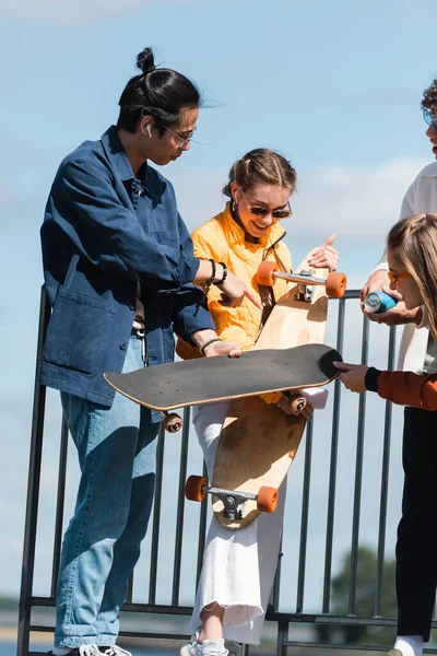 Asiático Hombre Apuntando Skateboard Cerca Sonriendo Amigos Aire Libre — Foto de Stock