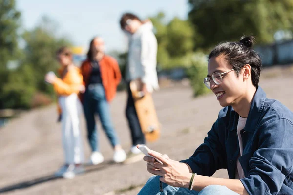 Happy Asian Man Eyeglasses Using Mobile Phone Blurred Friends — Stock Photo, Image