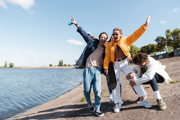 Şık giyimli neşeli ırklar arası arkadaşlar nehir kıyısında eğleniyorlar.