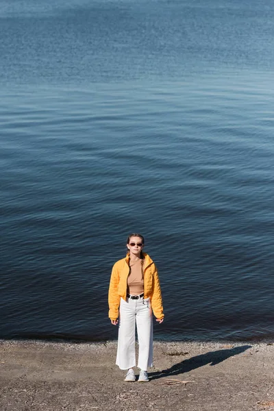 穿着太阳镜和时髦衣服站在河边的女人 — 图库照片