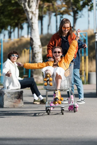 Lachende Frau Auf Rollschuhen Einkaufswagen Neben Glücklichen Multiethnischen Freunden — Stockfoto