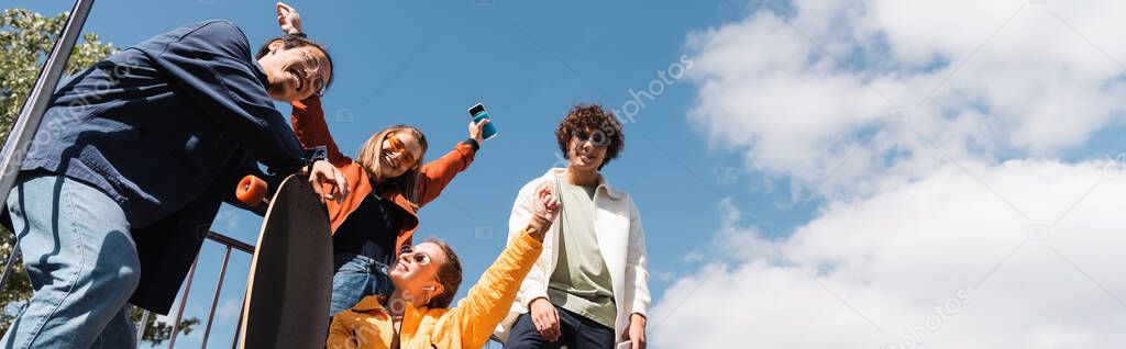 low angle view of happy women showing success gesture near interracial skaters, banner