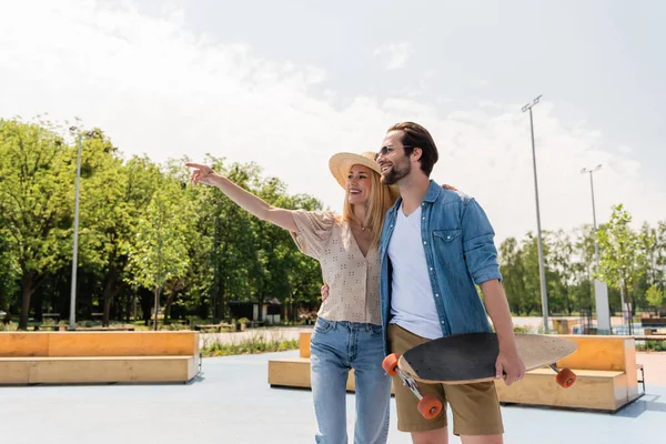 在滑板公园里 戴着太阳帽与长板拥抱男友的微笑的女人 — 图库照片
