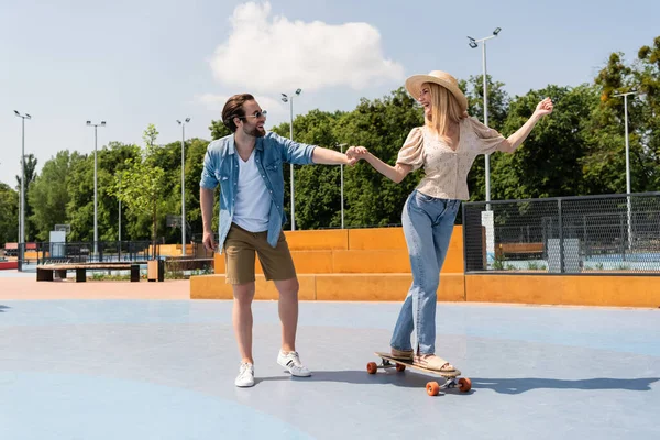 Pareja Positiva Cogida Mano Mientras Monta Longboard Skate Park —  Fotos de Stock