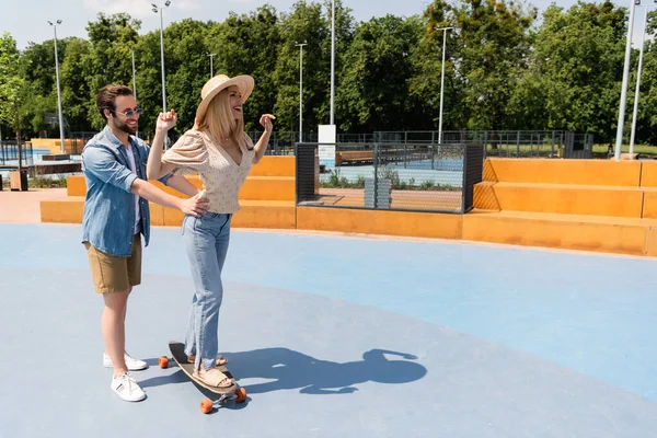 Hombre Sonriente Tocando Novia Sombrero Paja Montando Longboard Skate Park — Foto de Stock