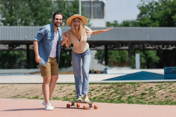 Pareja Positiva Cogida Mano Mirando Cámara Mientras Monta Longboard Skate —  Fotos de Stock