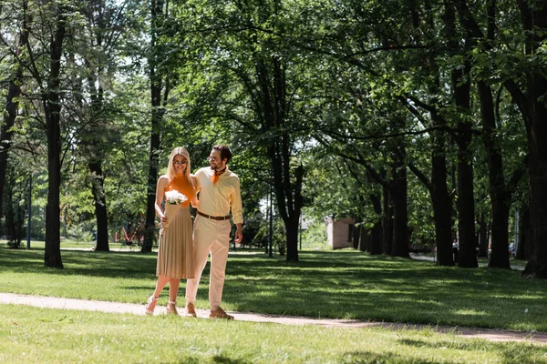 夏日公园里 戴着太阳镜 拿着花束的女人在男朋友身边微笑 — 图库照片