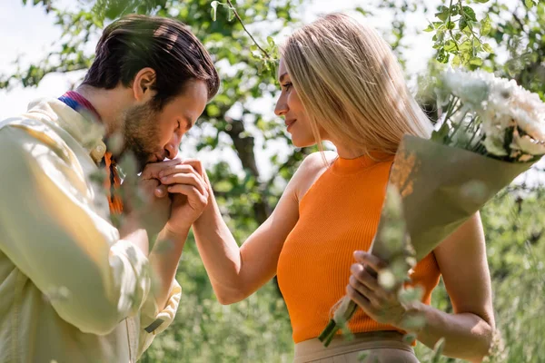 时尚男人在公园里亲吻女友手牵着花束的侧影 — 图库照片