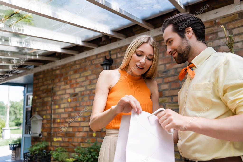 Stylish woman looking at shopping bag near stylish boyfriend in outdoor cafe 