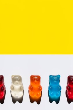 Close up view of colorful jelly bears on white and yellow surface clipart