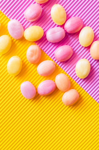 Top view of colorful sweets on textured pink and yellow background 