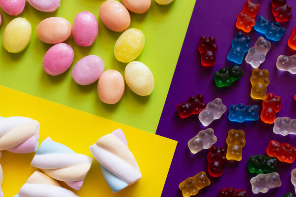 Flat lay of marshmallows near candies and jelly bears on colorful surface 