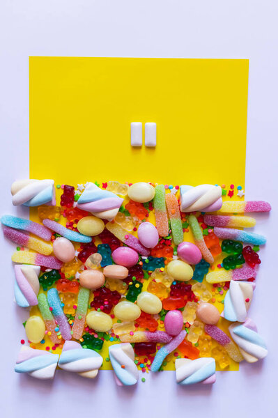Top view of chewing gums near colorful sweets on white and yellow surface 