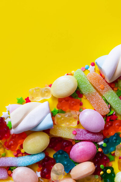 Flat lay with colorful jelly sweets and tasty marshmallows on yellow background 